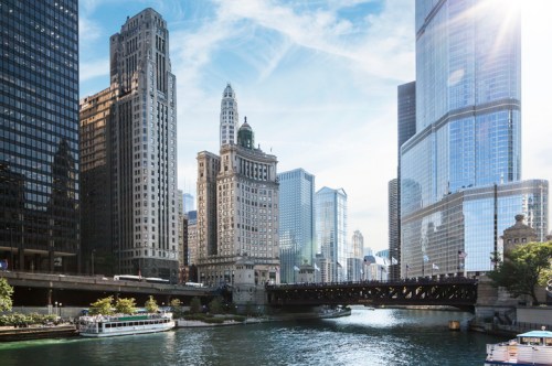 A scenic view of a river surrounded by tall buildings and a bridge, with a boat on the water under a clear sky.