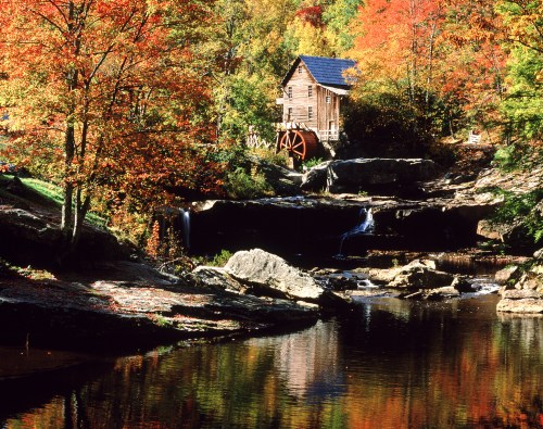 A scenic autumn landscape featuring a historic watermill beside a tranquil pond, surrounded by colorful fall foliage.
