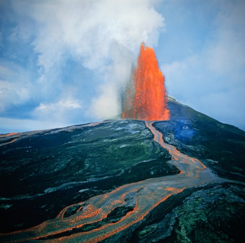 A volcano erupts, spewing lava and ash into the sky, with a flowing lava path down its side.