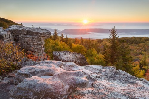 Sunrise over a mountainous landscape, with rocky outcrops and colorful autumn foliage in the foreground.