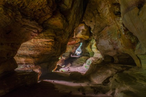 A colorful cave interior with textured rock formations and soft lighting illuminating the passageway.