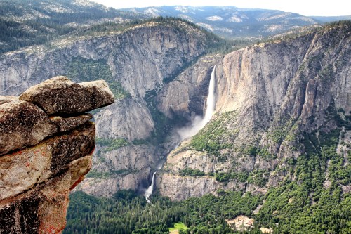 A stunning view of a waterfall cascading down rocky cliffs, surrounded by lush green forests and mountains in the background.