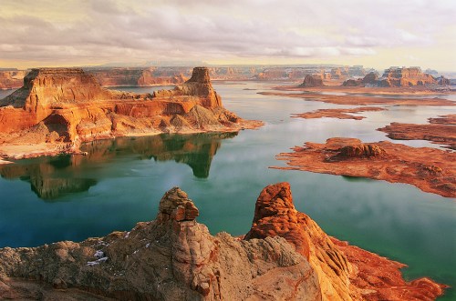 A scenic view of a vast lake surrounded by rocky cliffs and formations under a cloudy sky.