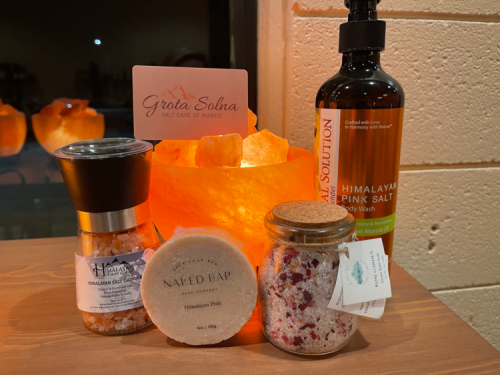 A collection of Himalayan salt products, including a salt lamp, bath salts, and body wash, arranged on a wooden surface.