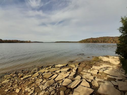 A serene lakeside view with rocky shorelines and distant trees under a cloudy sky.