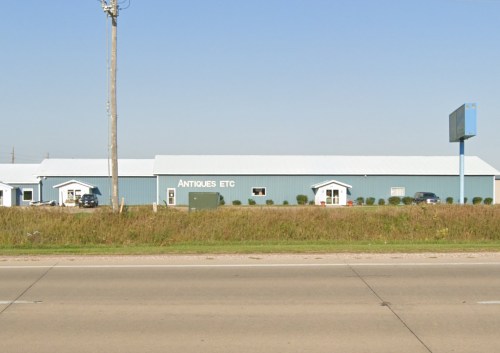 A large blue building with a sign reading "Antiques Etc." next to a highway, surrounded by grass and a clear sky.
