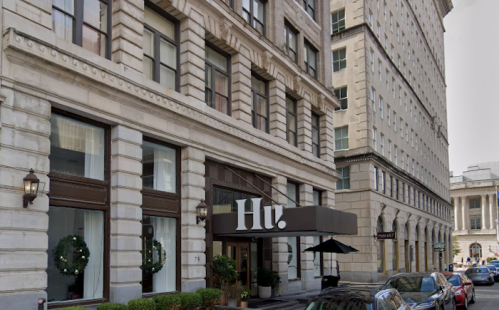 Exterior view of a building with "Hu." signage, featuring large windows and decorative wreaths, on a city street.