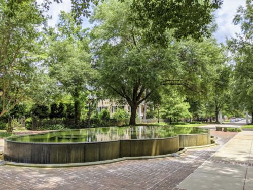 A serene park scene featuring a circular water feature surrounded by lush green trees and a paved walkway.