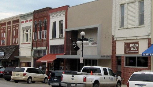 A street view of a small town with various shops and vehicles parked along the curb.