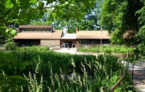 A modern building surrounded by greenery and trees, with a pathway leading to the entrance.
