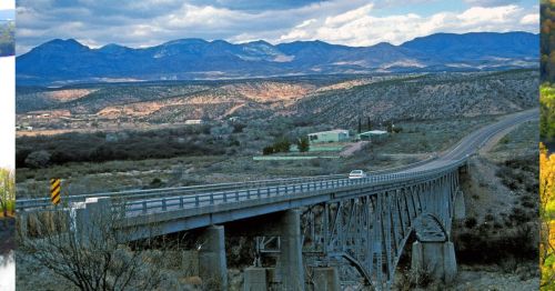 A bridge spans a valley with mountains in the background under a cloudy sky, showcasing a scenic landscape.