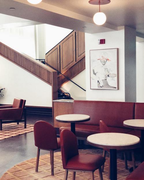 A modern café interior featuring red seating, round tables, and a staircase with a framed artwork on the wall.