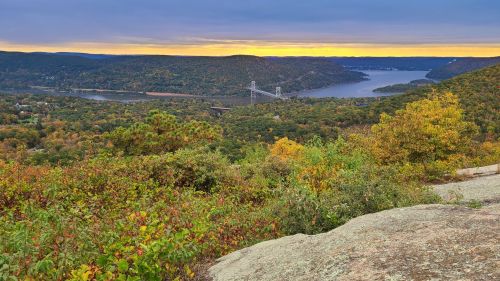 Scenic view of a river valley at sunset, surrounded by colorful autumn foliage and distant hills.