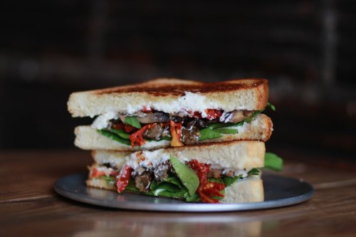 A toasted sandwich stacked with spinach, sun-dried tomatoes, and creamy filling on a metal plate.