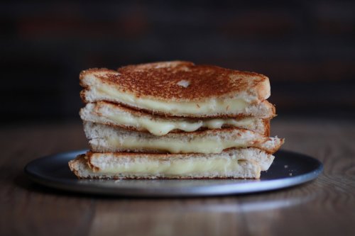 A stack of three golden-brown grilled cheese sandwiches on a silver plate, with melted cheese oozing between the layers.