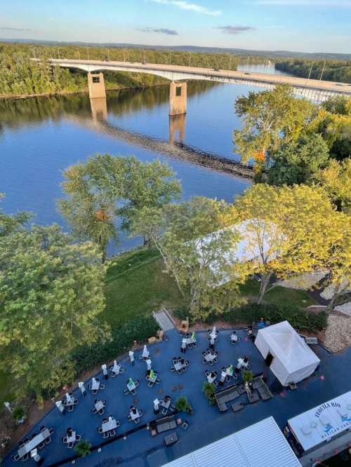 Aerial view of a river with a bridge, surrounded by trees and a patio area with tables and chairs.