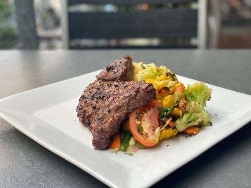 A plate featuring grilled steak alongside a colorful vegetable medley of cauliflower, broccoli, and tomatoes.