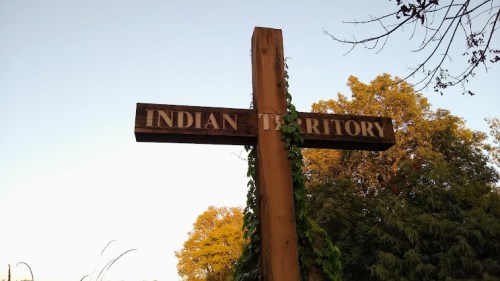 Wooden signpost reading "Indian Territory" with trees and a clear sky in the background.