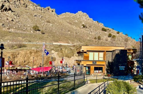 A scenic view of a building near a rocky hillside, with flags and a gathering area in the foreground.