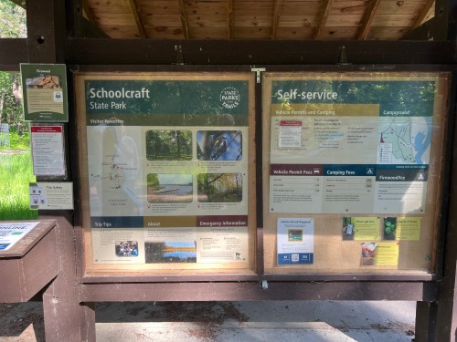 Information board at Schoolcraft State Park, detailing vehicle permits, camping fees, and park tips.