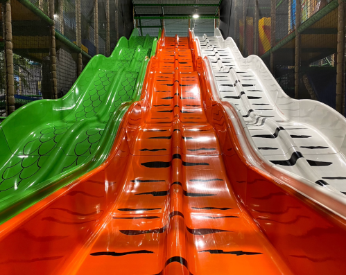 Colorful indoor slides in green, orange, and white, arranged side by side in a play area.