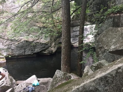 A serene natural scene featuring a dark pool of water surrounded by large rocks and trees.