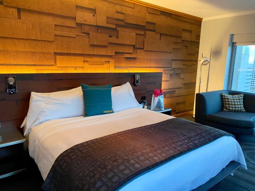 A modern hotel room featuring a king-sized bed, wooden accent wall, and a cozy seating area with a city view.