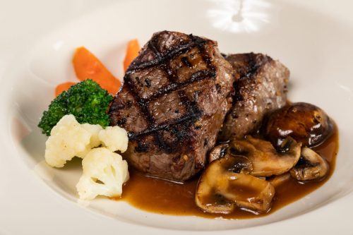 Grilled steak served with mushrooms, broccoli, cauliflower, and carrots on a white plate.