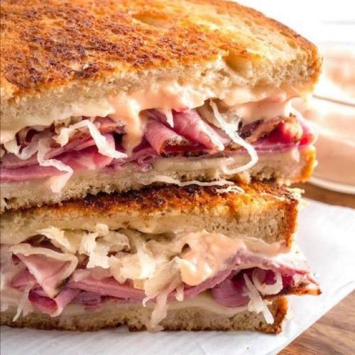 Close-up of a toasted sandwich filled with layers of ham, sauerkraut, and creamy sauce.