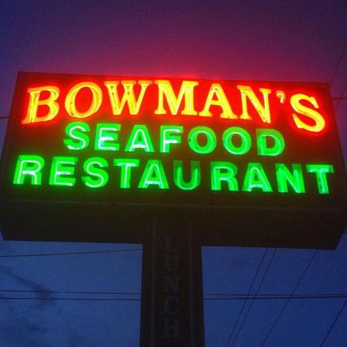 Neon sign for Bowman's Seafood Restaurant, glowing in red and green against a twilight sky.