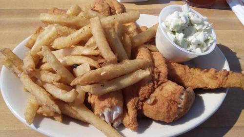 A plate of crispy fried chicken pieces served with golden French fries and a side of coleslaw in a cup.