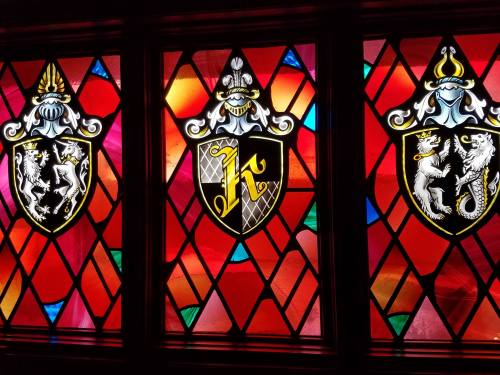 Stained glass window featuring three heraldic shields with colorful diamond patterns.