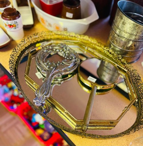 A decorative mirrored tray with an ornate handle, surrounded by various containers and colorful items in the background.