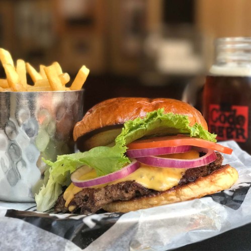 A juicy cheeseburger with lettuce, tomato, and onion, served with fries and a cold drink in the background.