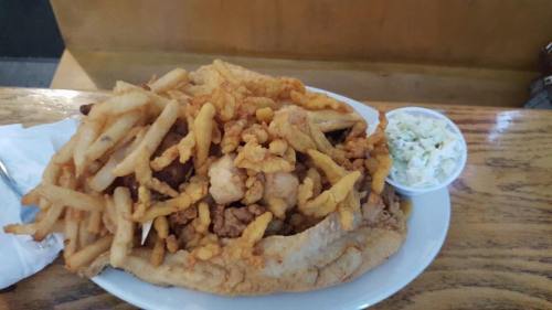A large plate of fried seafood and chicken topped with crispy onions, served with a side of coleslaw and fries.