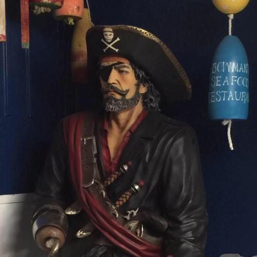 A life-sized pirate statue with an eye patch, wearing a hat and coat, surrounded by nautical decor.