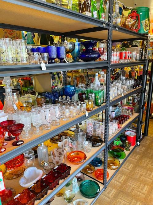 A display of colorful glassware and decorative items on shelves in a vintage shop.