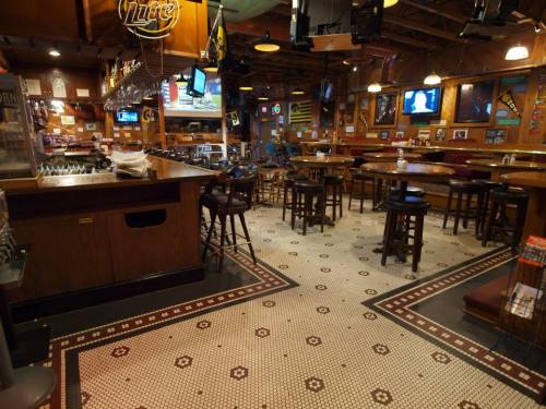 A cozy bar interior with wooden furniture, a tiled floor, and multiple TVs displaying sports.