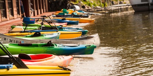 Colorful kayaks lined up along a calm waterway, with a dock and greenery in the background.