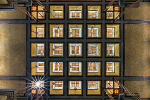 A geometric ceiling with a grid of windows, illuminated by a central light, showcasing architectural details.