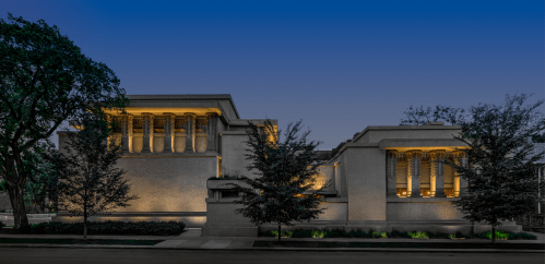 A modern building with illuminated architectural features, surrounded by trees at dusk.