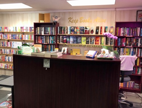A cozy bookstore interior with shelves of books, a wooden counter, and a sign that says "Keep Books Alive."