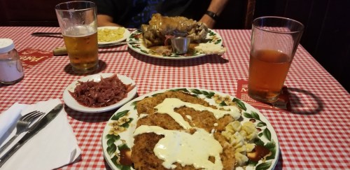 A table set with two plates of food, including fried chicken, coleslaw, and a side of meat, with drinks in glasses.