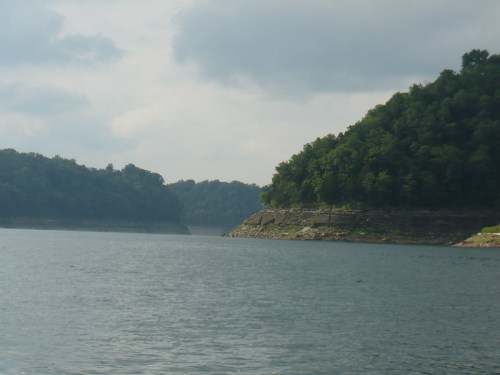 A serene lake surrounded by lush green hills under a cloudy sky.