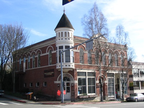 Historic brick building with a turret, large windows, and decorative trim, set against a clear blue sky.