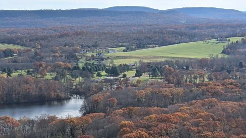 A scenic view of rolling hills and a lake, surrounded by autumn foliage in vibrant orange and yellow hues.