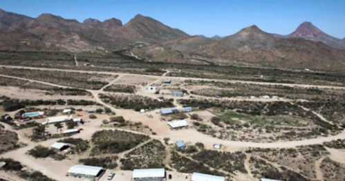 Aerial view of a desert landscape with scattered buildings and winding roads, surrounded by mountains.