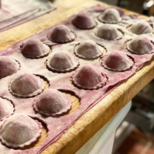 A wooden surface with rows of purple-hued ravioli dusted with flour, ready for cooking.