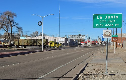 A view of a road entering La Junta, Colorado, with a city limit sign and buildings along the street.