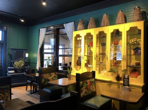 Cozy café interior featuring colorful furniture, a yellow display cabinet, and green walls with plants and decorative items.
